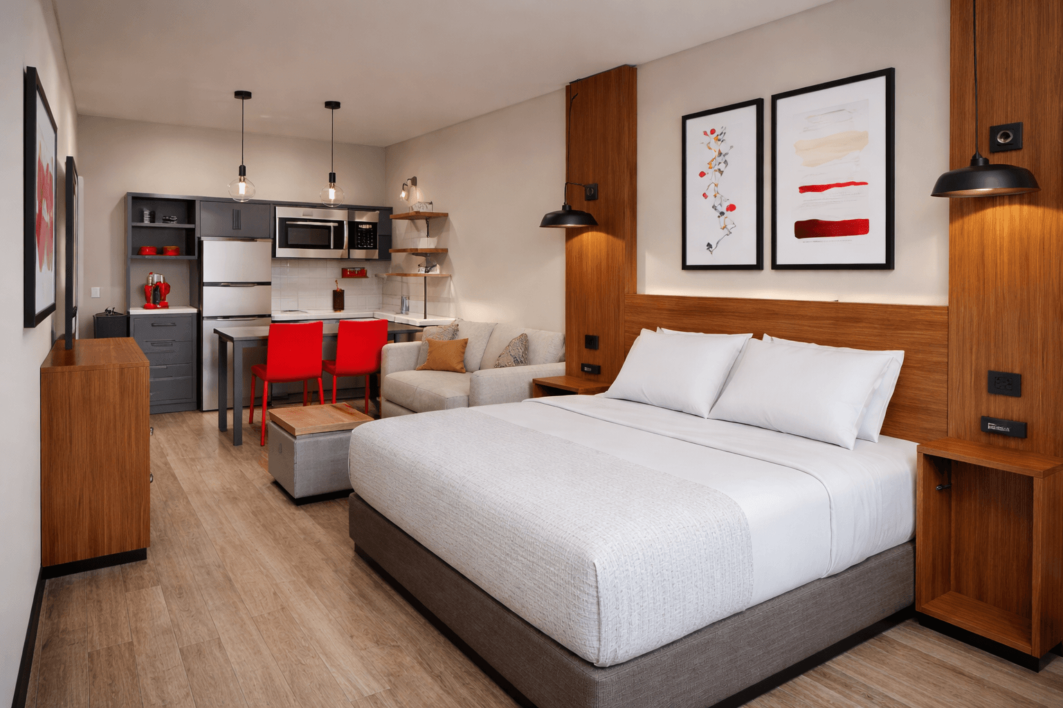 Hawthorn Suites studio guest room with integrated headboard millwork, kitchenette, living area, and red accent furniture.
